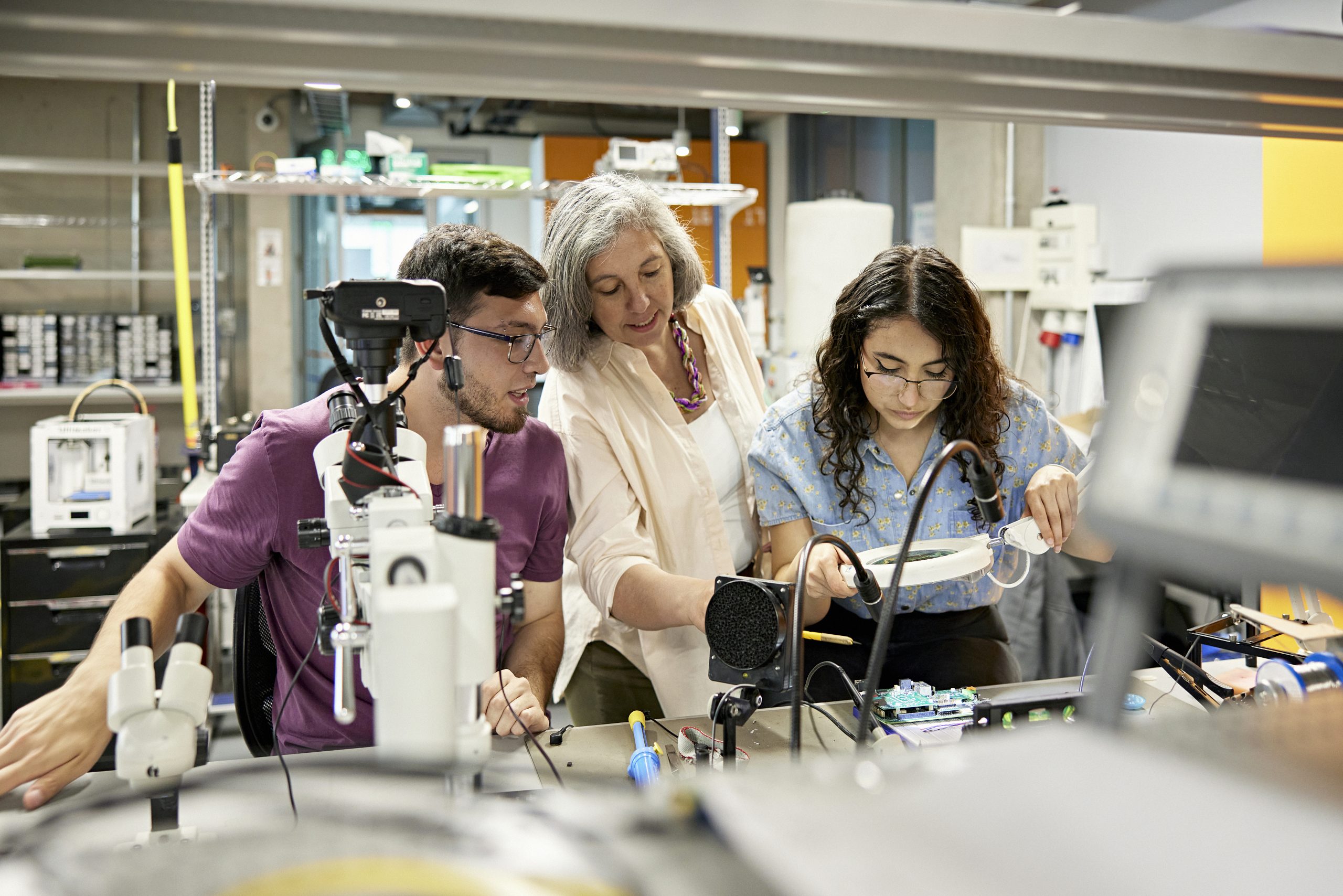 Waist-up view of mature educator assisting young lab partners as they work on project in technical college training class.